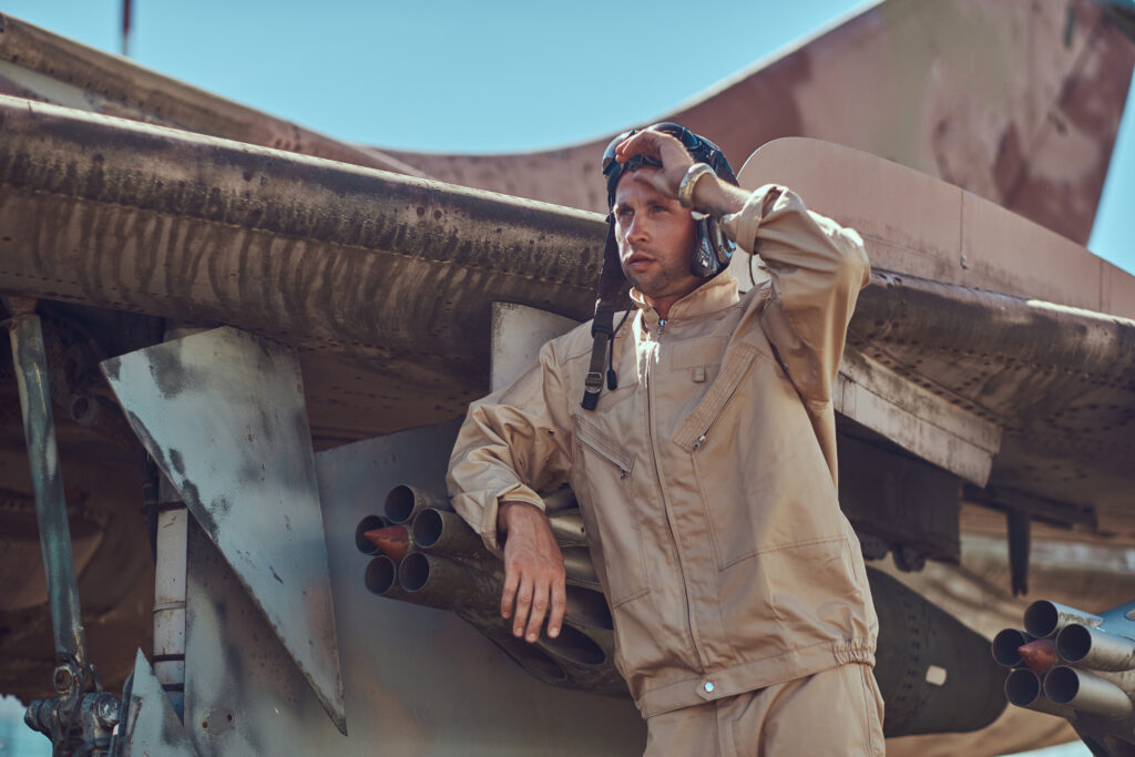 Home 5 pilot in uniform and flying helmet standing near an old war fighter interceptor in an open air museum.